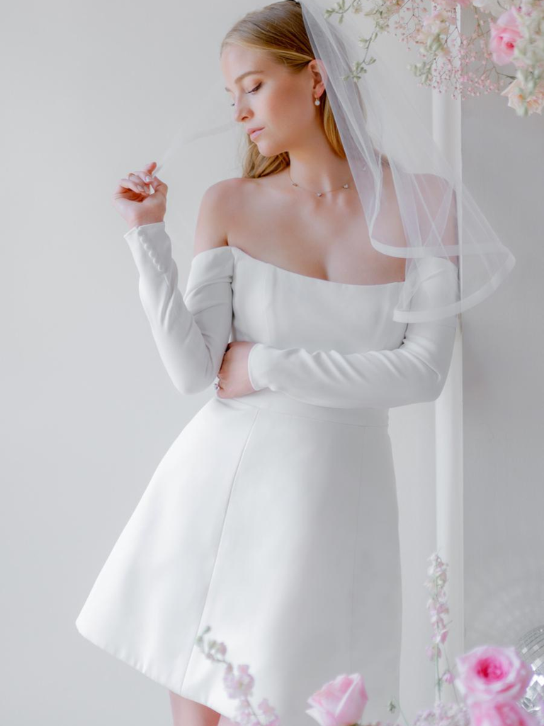 Model poses in white long-sleeved mini dress and veil.
