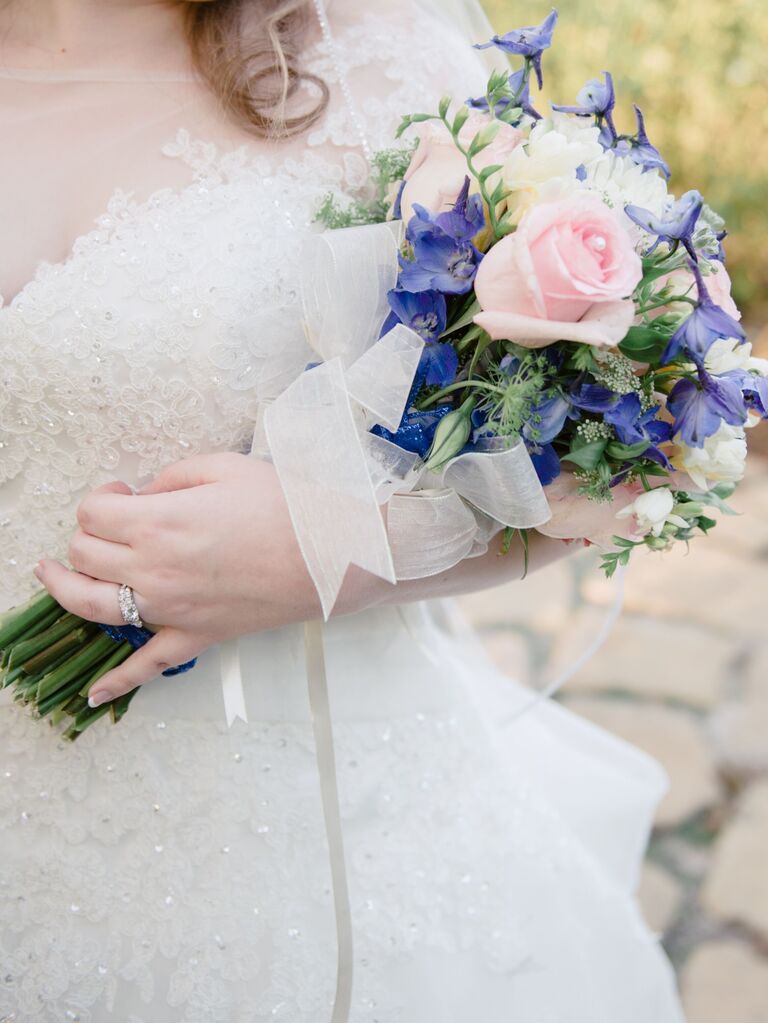 bride holding pageant style wedding bouquet with pink long stem roses and blue delphinium