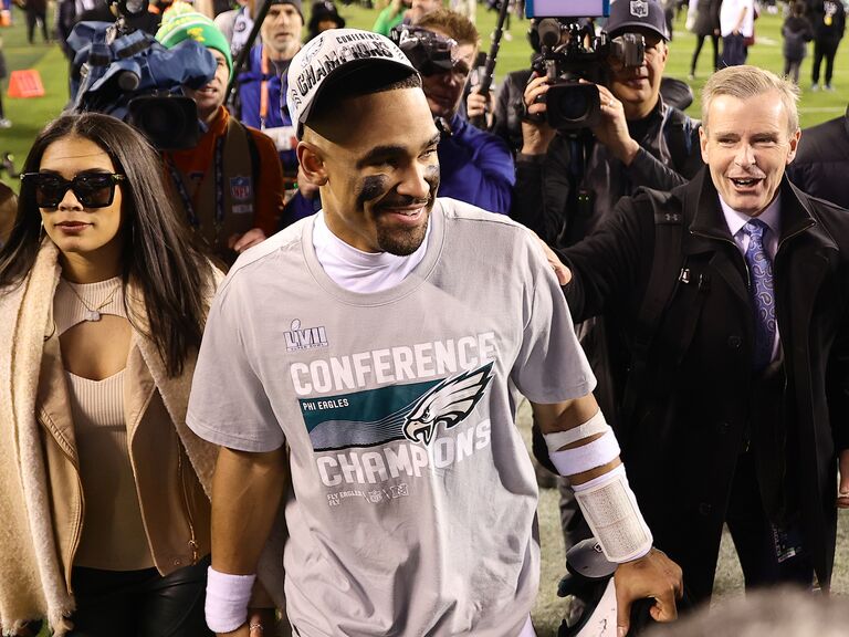 Jalen Hurts smiles and walks off the field hand in hand with a woman while reporters film. 