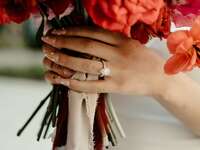Hand wearing engagement ring and holding bouquet