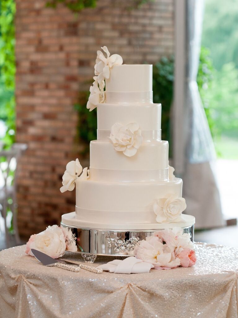 A four-tiered all-white wedding cake with elegant white sugarcraft flowers