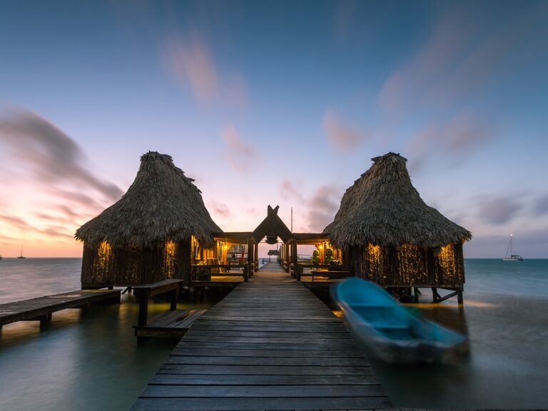 A boardwalk in Ambergris Caye with a gorgeous sunset behind wooden structures. 