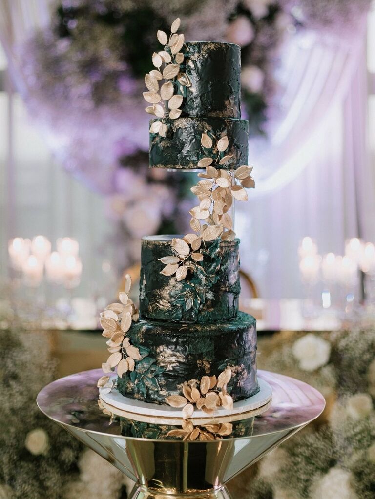 A four-tiered dark wedding cake with gold sugarcraft greenery