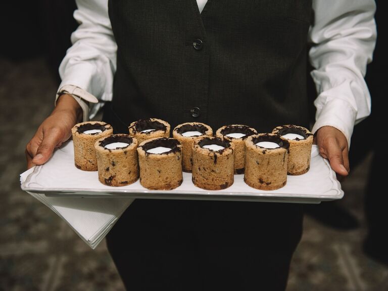 Server holds a tray of milk and cookie shooters. 