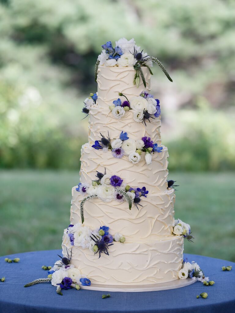five tier white wedding cake decorated with blue, white and purple flowers
