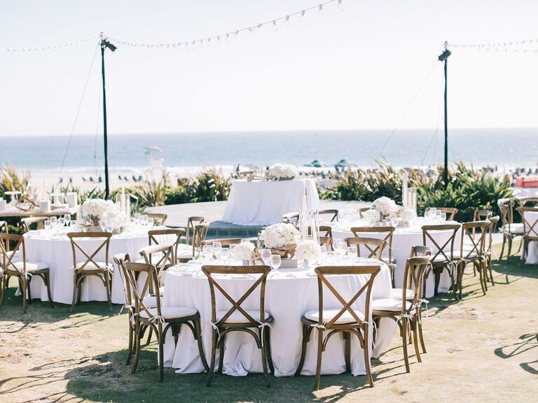 beach wedding reception with round tables and wooden cross back chairs beneath strands of bistro lights