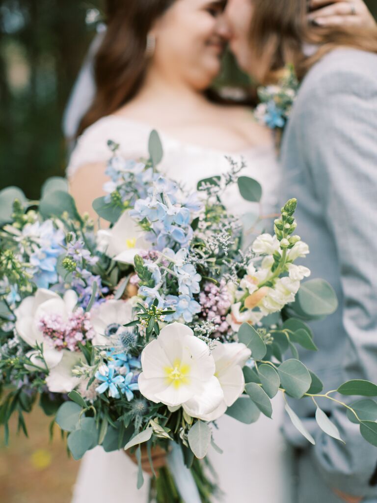 bride holding pastel blue, pink, purple and white wedding bouquet